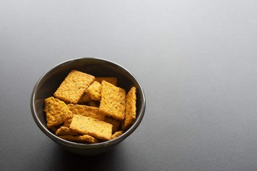 Top view of a brown plate filled with crackers on a black table.Sunny day. Copy space for text.