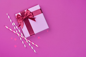 Purple classic gift box with shiny satin bow and cocktail straws with confetti in the shape of stars as attributes of party