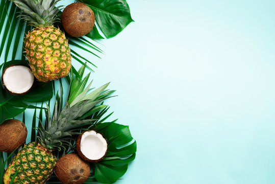 Exotic pineapples, ripe coconuts, tropical palm and green monstera leaves on blue background with copyspace for your text. Creative layout. Summer concept. Flat lay, top view