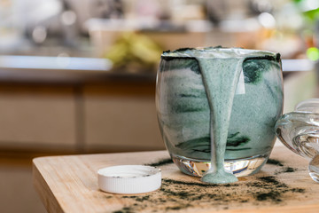 Closeup view fresh kefir probiotik drink in clear glass mixed with green spirulina powder on kitchen table