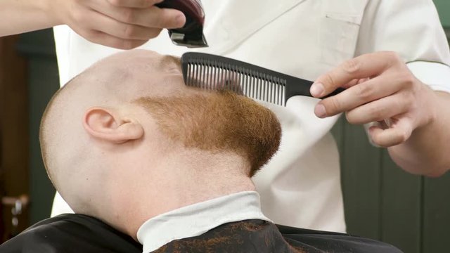 Shaving of beard. Barber cutting men's face hair with beard trimmer at barbershop. 4K
