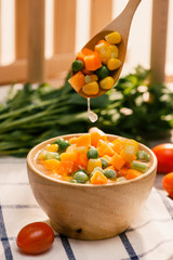 Ladle of steamed freshly harvested young vegetables including crinkle cut sliced carrots, peas and...