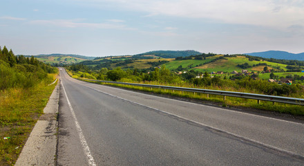 The mountain road runs along the village, fields and green slopes under the gray sky. a place for recreation and tourism