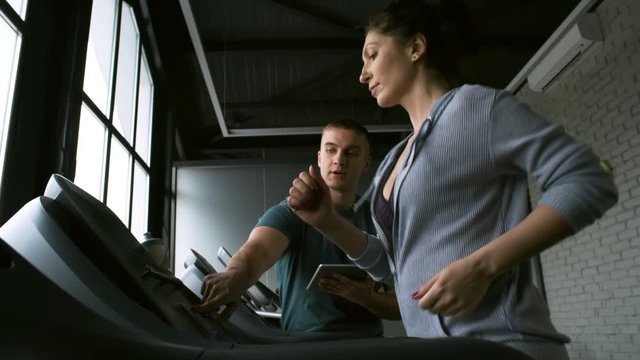 Side view of concentrated woman listening to male instructor when working out on treadmill at the gym