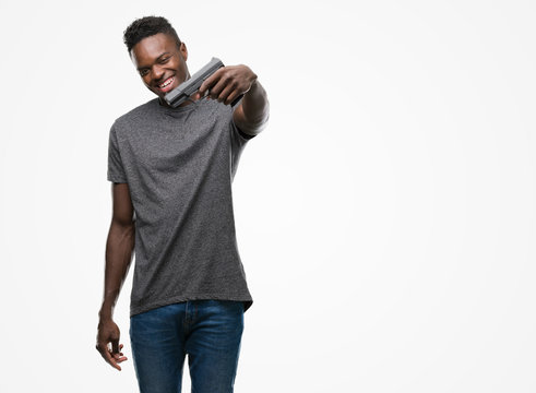 Young african american man holding a gun with a happy face standing and smiling with a confident smile showing teeth