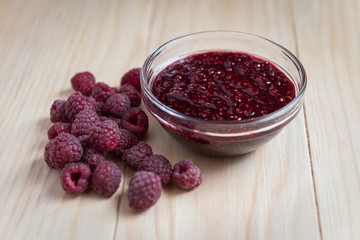 Homemade Raspberry jam in a glass bowl with fresh ripe organic Raspberries  on a wooden table