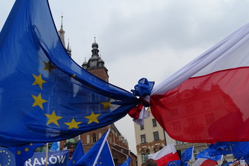 Związana flaga Unii Europejskiej i Polski, demonstracja w Krakowie, widoczna część napisu Kraków, w tle architektura rynku, wieże kościoła mariackiego