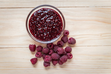 Homemade Raspberry jam in a glass bowl with fresh ripe organic Raspberries  on a wooden table