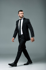 handsome businessman in suit walking and looking away on grey