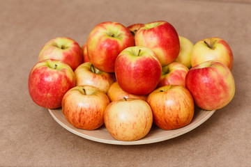 large plate of red-yellow apples on brown background,