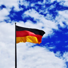German national flag waving on wind on bright blue cloudy sky background in Berlin.