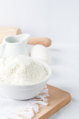  Baking ingredients. White background. Ingredients and tools to make a cake. Flour, milk, eggs, rolling pin, wooden spoons, jar. Copy space. Bakery. Baking concept