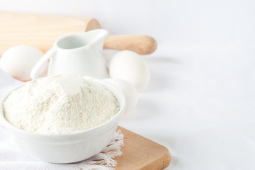  Baking ingredients. White background. Ingredients and tools to make a cake. Flour, milk, eggs, rolling pin, wooden spoons, jar. Copy space. Bakery. Baking concept