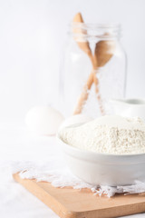  Baking ingredients. White background. Ingredients and tools to make a cake. Flour, milk, eggs, rolling pin, wooden spoons, jar. Copy space. Bakery. Baking concept