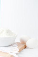  Baking ingredients. White background. Ingredients and tools to make a cake. Flour, milk, eggs, rolling pin, wooden spoons, jar. Copy space. Bakery. Baking concept
