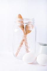  Baking ingredients. White background. Ingredients and tools to make a cake. Flour, milk, eggs, rolling pin, wooden spoons, jar. Copy space. Bakery. Baking concept