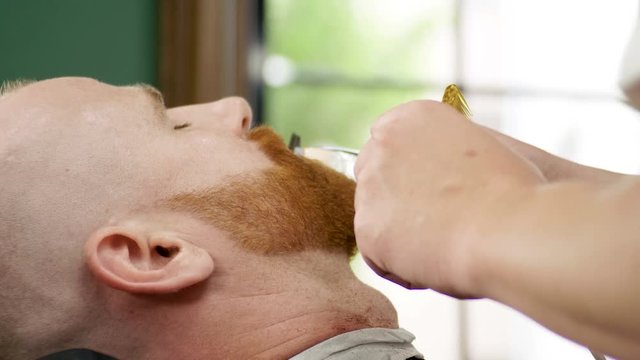 Shaving of beard. Barber cutting men's face hair with beard trimmer at barbershop. 4K