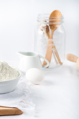 Fototapeta na wymiar Baking ingredients. White background. Ingredients and tools to make a cake. Flour, milk, eggs, rolling pin, wooden spoons, jar. Copy space. Bakery. Baking concept
