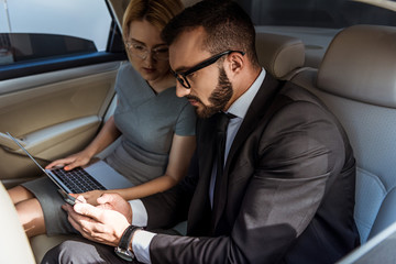 handsome businessman showing something on smartphone to assistant in car