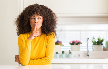 Fototapeta na wymiar African american woman wearing yellow sweater at kitchen asking to be quiet with finger on lips. Silence and secret concept.