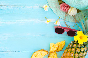 Concept of tropical fruit. Pineapple, flowers, sunglasses and straw hat on wood plank blue color. Summer vacation background and top view design
