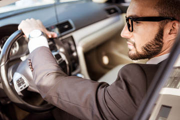 side view of handsome driver in suit and glasses driving car