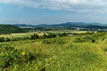 View from the hill to a small rural village in the background of green mountains and the endless blue sky