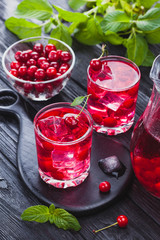 Red cherry cocktail with ice and fresh mint on a black wooden table