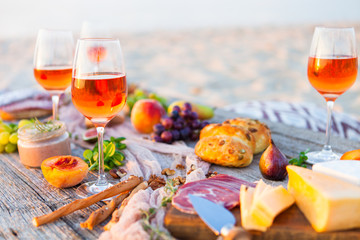 Picnic on beach at sunset in boho style. Romantic dinner, friends party, summertime, food and drink concept - 211900283
