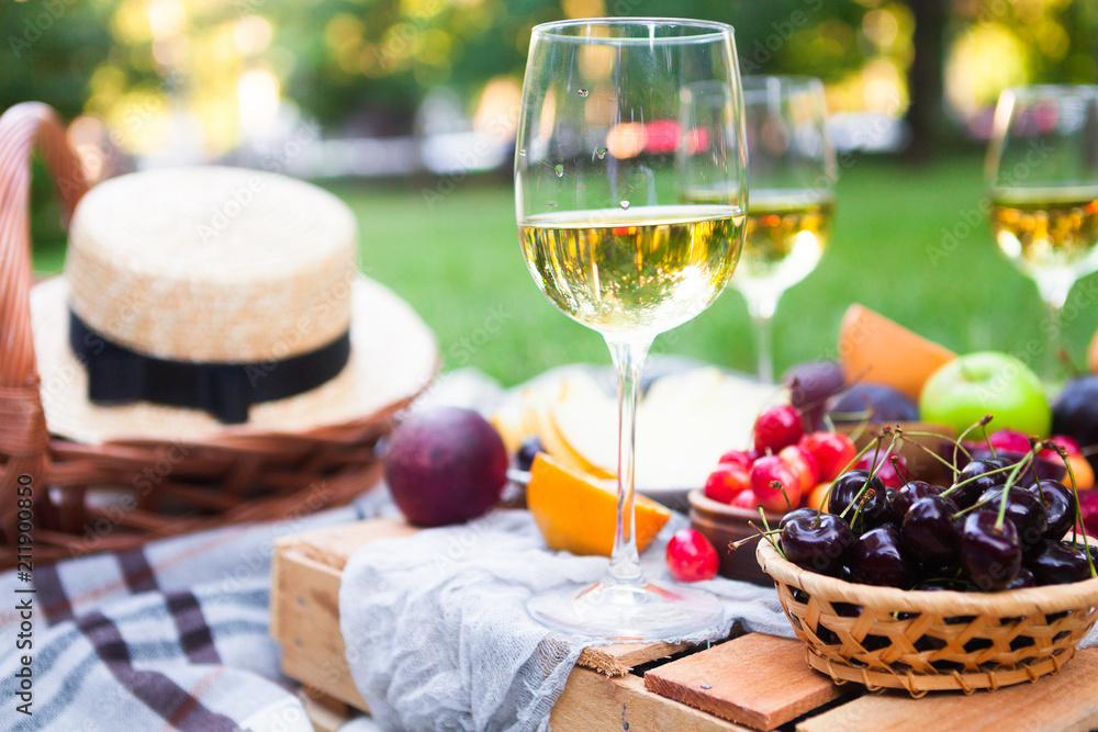 Wall mural picnic background with white wine and summer fruits on green grass, summertime party