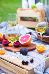 Picnic background with white wine and summer fruits on green grass, summertime party