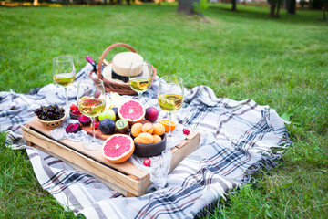 Picnic background with white wine and summer fruits on green grass, summertime party