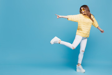 Obraz premium Pretty young woman in yellow sweater posing on blue background. Attractive woman pointing fingers to the left with cheerful and happy expression. Copy space.