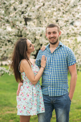 Young couple in love resting in the blooming garden. white blooming trees