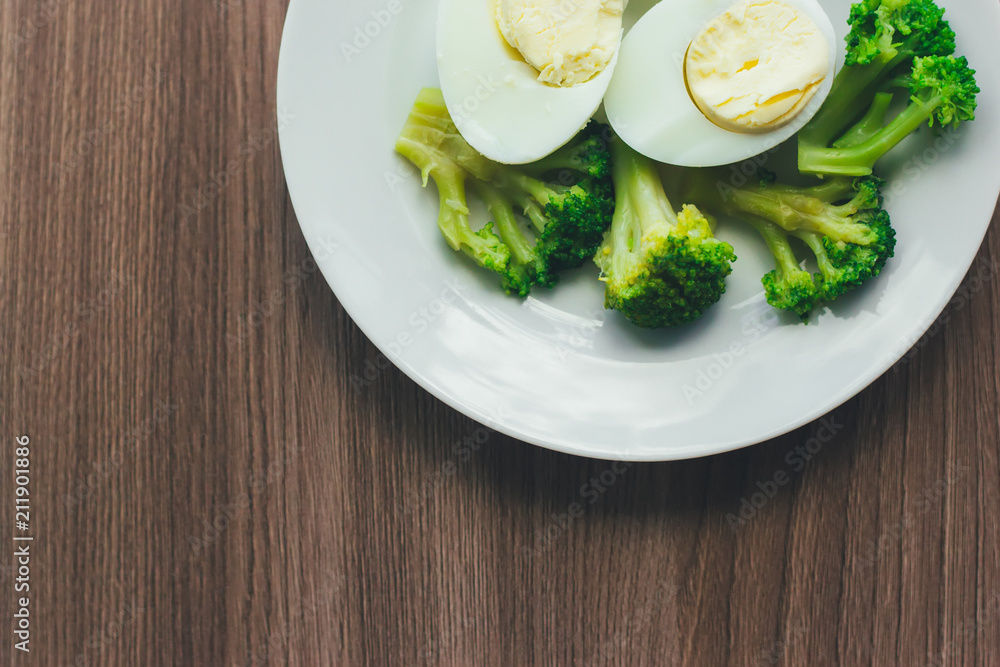 Wall mural boiled eggs and broccoli on a white plate on a wooden table.