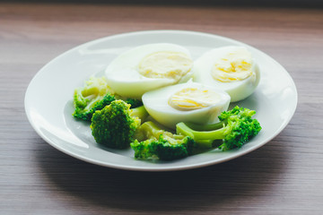 Boiled eggs and broccoli on a white plate on a wooden table.