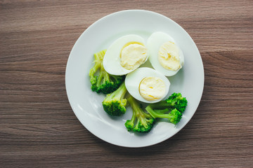 Boiled eggs and broccoli on a white plate on a wooden table.