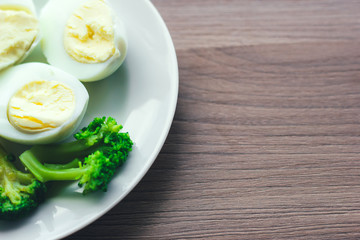 Boiled eggs and broccoli on a white plate on a wooden table.