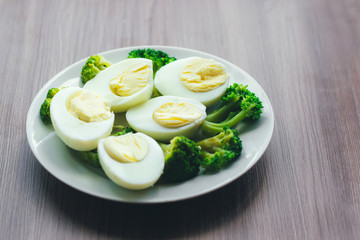 Boiled eggs and broccoli on a white plate on a wooden table.