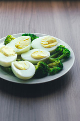Boiled eggs and broccoli on a white plate on a wooden table.