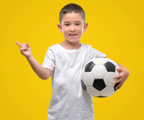 Dark haired little child playing with soccer ball very happy pointing with hand and finger to the...