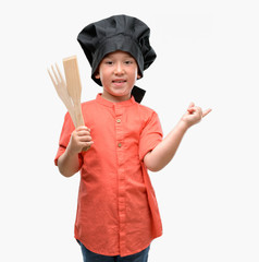 Fototapeta premium Dark haired little child wearing chef uniform very happy pointing with hand and finger to the side
