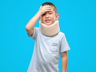 Dark haired little child injured wearing neck collar stressed with hand on head, shocked with shame and surprise face, angry and frustrated. Fear and upset for mistake.