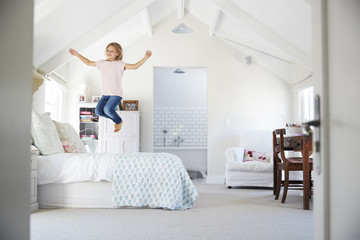 Happy young girl jumping on bed in her bedroom