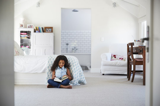 Young black girl reading a book alone in her bedroom
