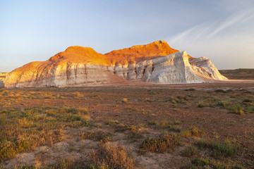 Multicolored red, orange and yellow single hill on the grass-covered steppe at sunset in Eastern...