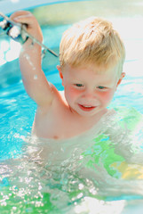 Fototapeta na wymiar Baby with toy plane in swimming pool. Little boy learning to swim in outdoor pool. Swimming with kids. Healthy sport activity for children. Sun protection swim wear. Water toys.