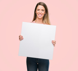 Beautiful young woman holding advertising banner with a happy face standing and smiling with a...
