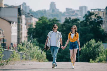 Happy couple of hipster buskers walking and holding hands at city street