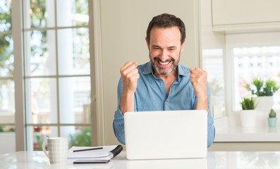 Middle age man using laptop at home screaming proud and celebrating victory and success very...